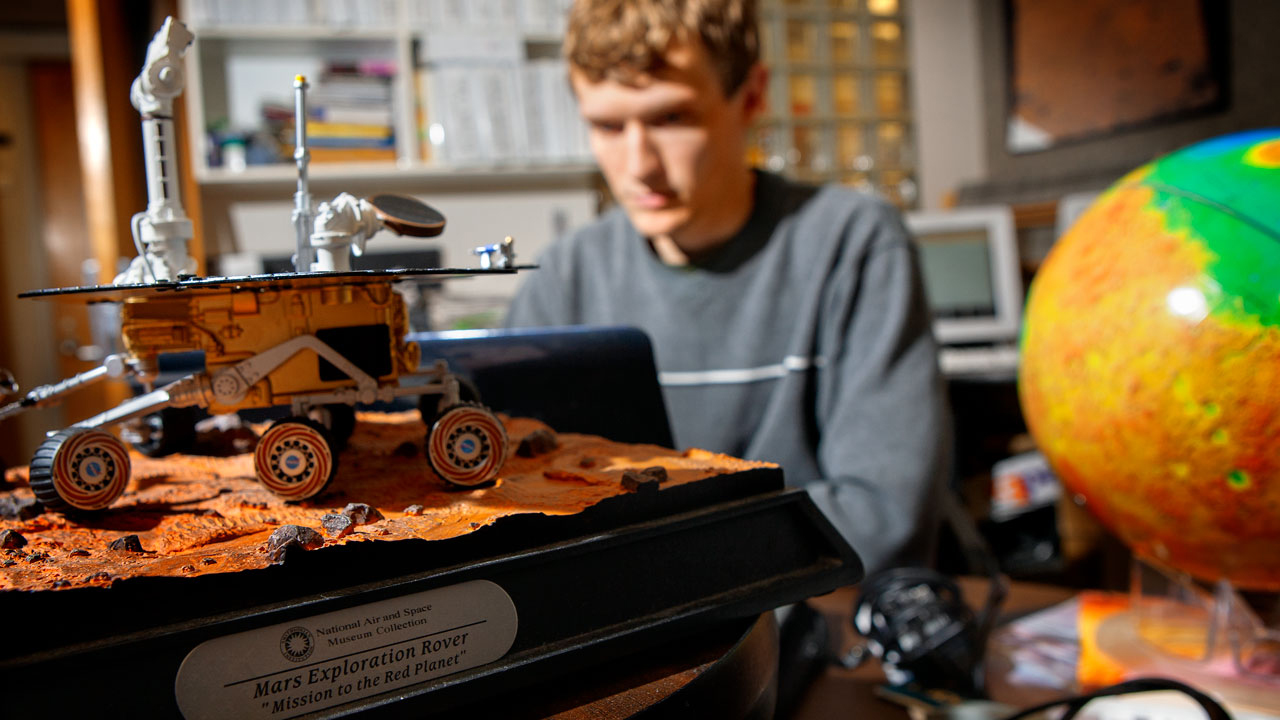 Student works on computer with model of Rover in foreground