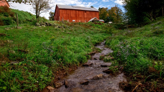 A red barn with a brook in the foreground.