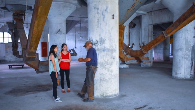 Two students and a man stand in an industrial building