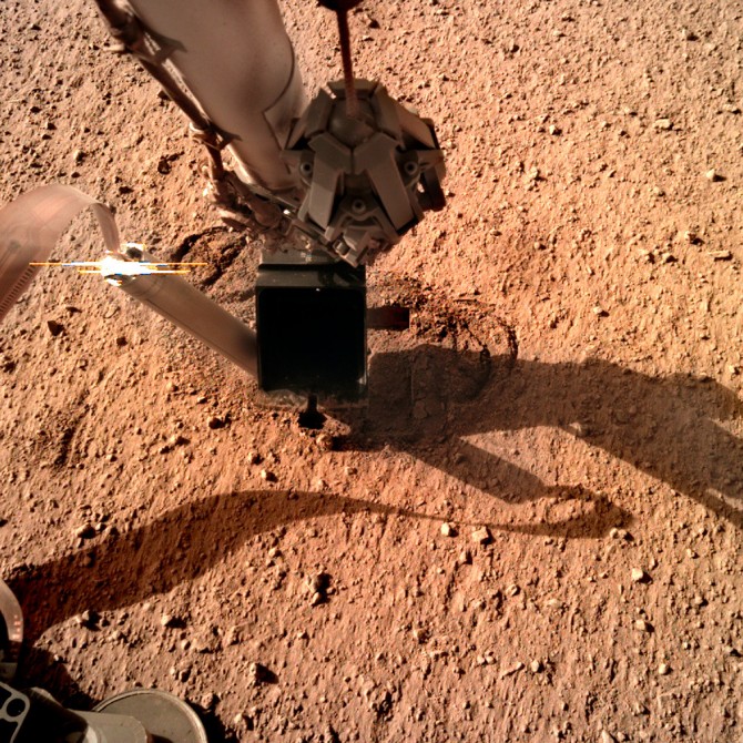 The NASA InSight lander stretches out its robotic arm into the Mars’ dusty soil.