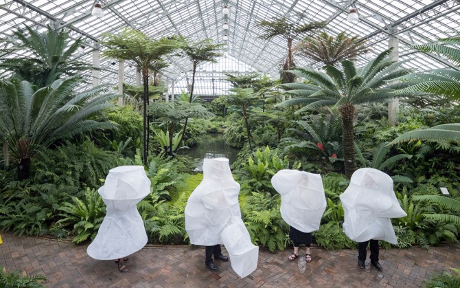 A greenhouse with people draped in white net sculptures.