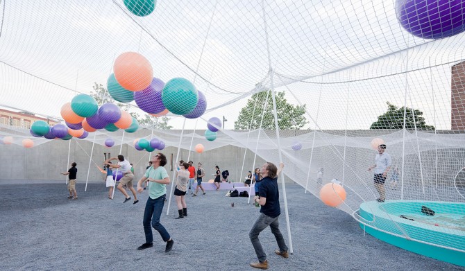 People standing underneath a giant net with colorful balls on top.
