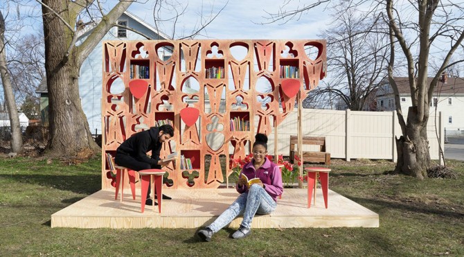 A wooden structure containing books with people sitting and reading in front.