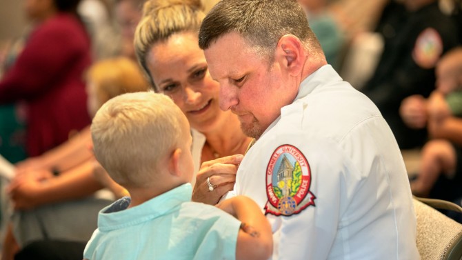Lt. Jeffery Montesano's wife, Maria, fixes his pin while he holds their grandson at the ceremony.