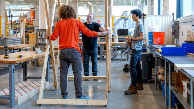 A dragon begins to take shape in Rand Hall as Andrew Sandberg ’28, left, and Ming-Huei Fisher ’28, right, begin assembling the structure, supported by Kurt Brosnan, AAP’s material practice facilities shop manager.