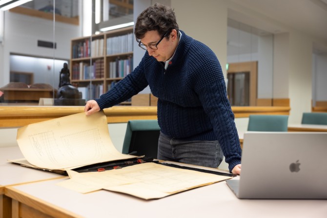 Person turns large pages of a yellowed document in a library setting