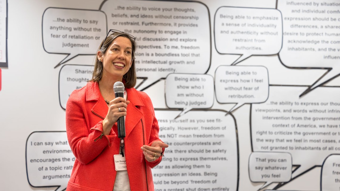 Woman holds mic in front of backdrop with speech bubbles