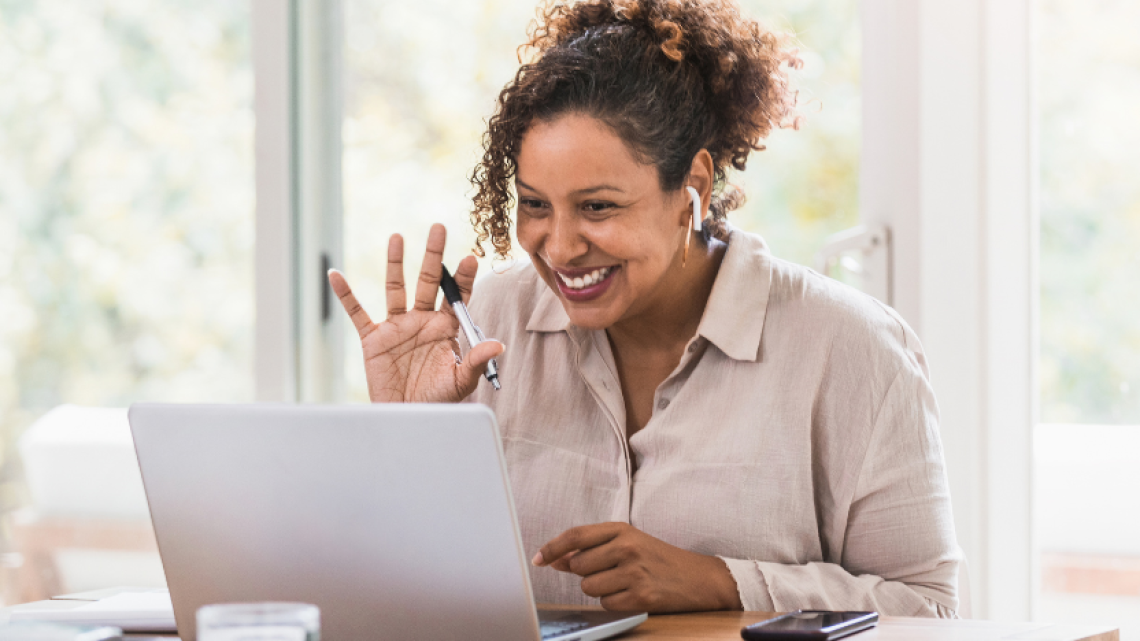 woman waving and smiling at laptop during online meeting