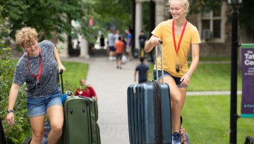 Two young women carrying suitcases upstairs. 