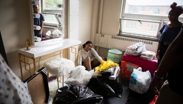 Smiling young woman sitting in corner surrounded by unpacked boxes and bags.