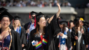 A graduate waves as she enters the stadium. 
