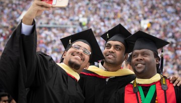 Three graduates take a selfie in the stadium. 