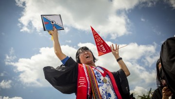 A graduate cheers, holding a pennant and mortarboard. 