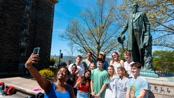 A class gathers for a group photo next to the Ezra Cornell statue.