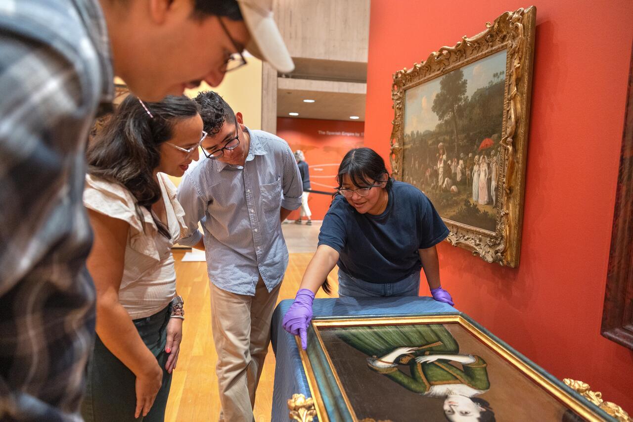 Three students gather around a portrait with a curator
