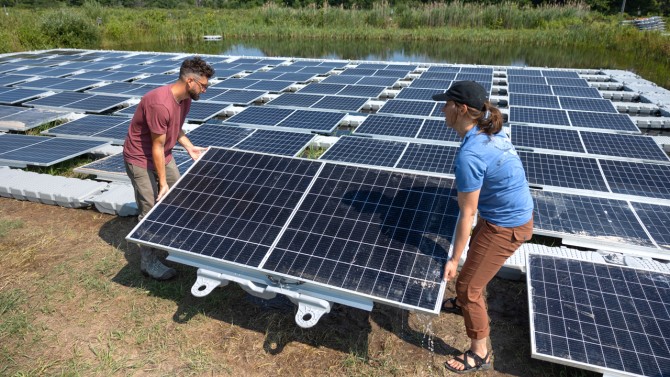 Adding solar panels to a pond in July, Steve Grodsky, left, and doctoral student Caitlin Davis aim to understand how floating photovoltaic panels affect the biology of the water.