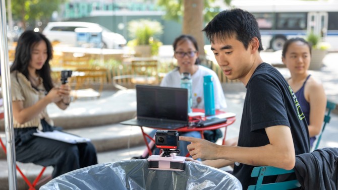 Doctoral student Frank Bu, foreground, checks the camera on one of the trashbots during deployment in Albee Square, Brooklyn, in July. Also pictured, left to right, are team members Nicole Sin ’26, JiaYing Li ’25 and Melina Tsai, a 2023 graduate of Cooper Union.