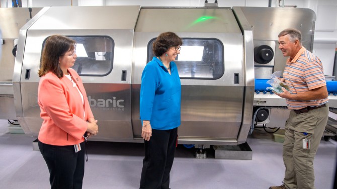   Extension support specialist John Churey, right, discusses the Hiperbaric high-pressure processing unit (HPP) with Olga Padilla-Zakour, professor and chair of the Department of Food Science, left, and President Martha E. Pollack, center