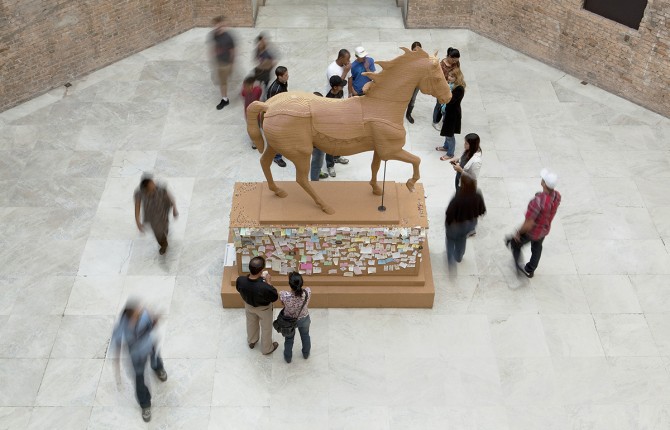 A wooden horse with notes attached to the base surrounded by people.