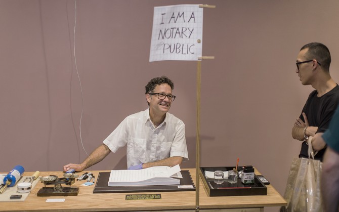 A person sitting at a desk with a sign that reads 'I am a notary public'
