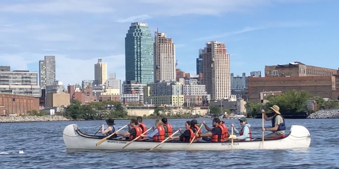 People in a canoe next to a city skyline.