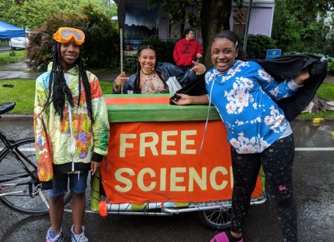 Three kids stand around a table with a banner reading, "Free Science"