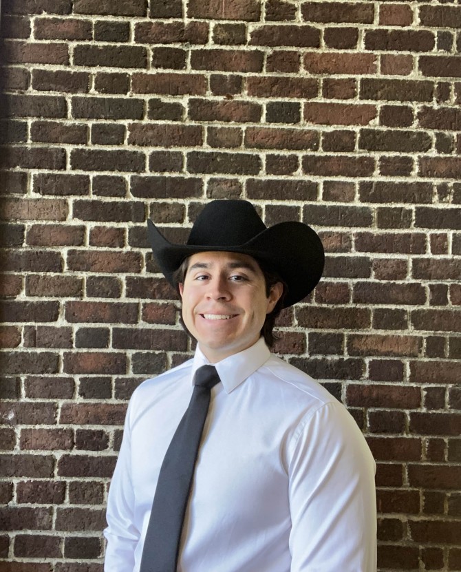 Michael Sanchez stands against a brick wall in a black cowboy style hat