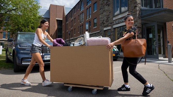 Two women push a moving box.