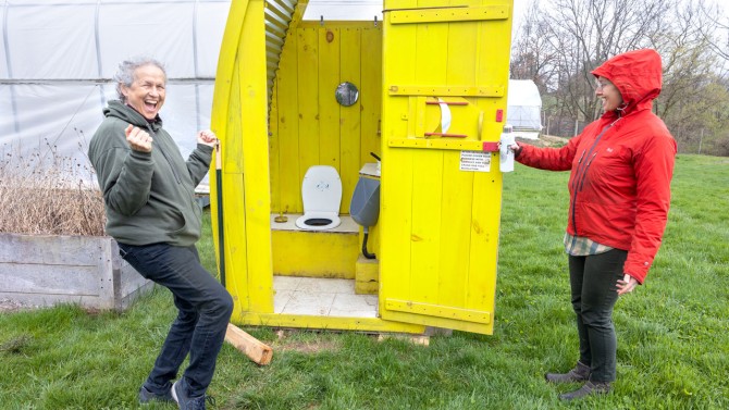 Rebecca Nelson, professor of plant science and global development in the College of Agriculture and Life Sciences, and postdoctoral researcher Krisztina Mosdossy show off an “eco loo” source-separating toilet at the Dilmun Hill Student Farm.