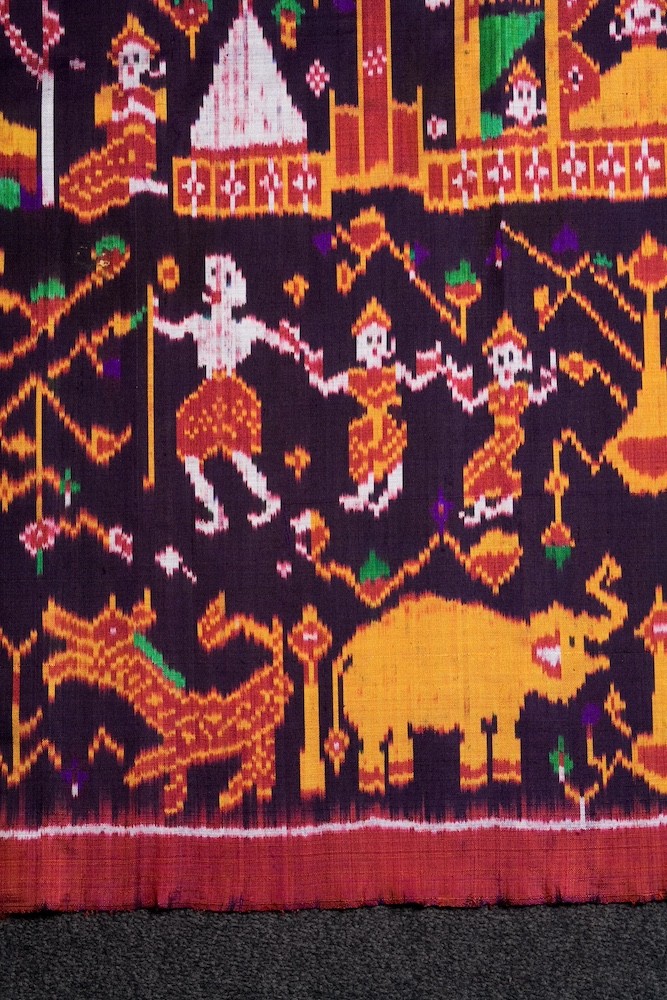 Detail of a woven cloth showing figures dressed in red and yellow