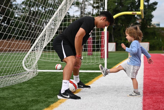 Cornell men’s soccer player Fernando Garate stands in the goal as young children attempt to score.