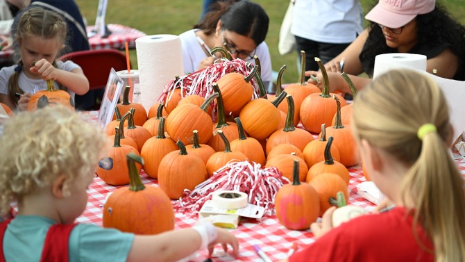 Families and Cornell students decorate small pumpkins with colored markers and stickers at the arts & crafts station.