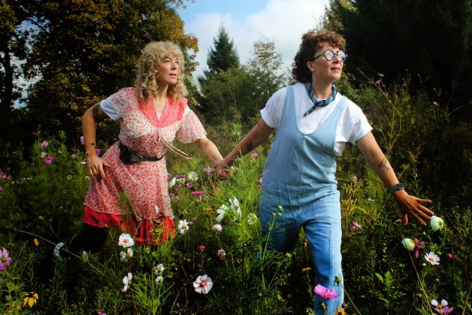 Two people -- characters in a play -- walk thorugh a field of flowers, holding hands