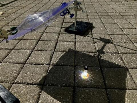 Contraption set up on a sunny brick patio, focusing sunlight on a glass vial