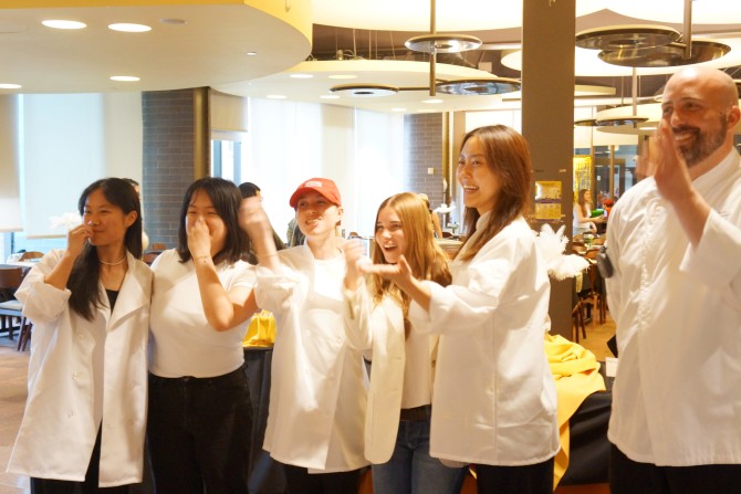Students in white chef's coats encourage their 600-800 guests to eat at their themed dinner experience.