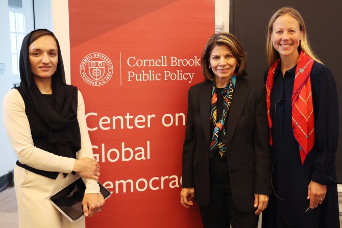 Zarifa Ghafari, former Costa Rican President Laura Chinchilla, and Professor Rachel Riedl stand together in front of a red Center on Global Democracy banner 