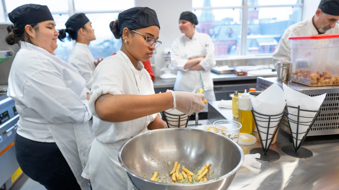 Chef assistant Nicole Beamon '26, a hotel administration major in the Cornell Peter and Stephanie Nolan School of Hotel Administration, prepares an order of truffle fries in the new full-service kitchen space of the Grailer Food Lab.