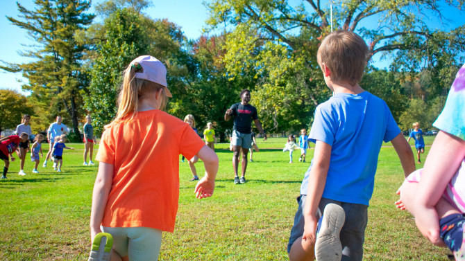 Ailemen ’26 leads a group of children through a stretching exercise.