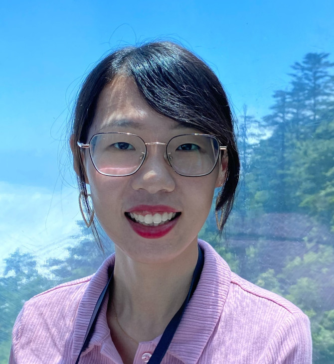Jiameng Lai stands in front of a window looking out into a wooded area
