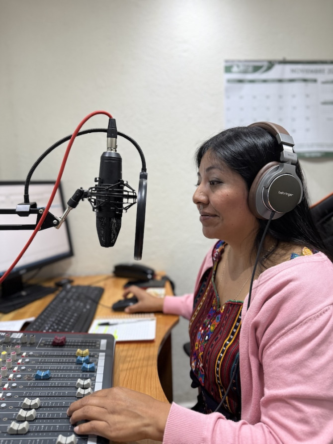 Person wearing large headphones speaks into a microphone while operating a sound board