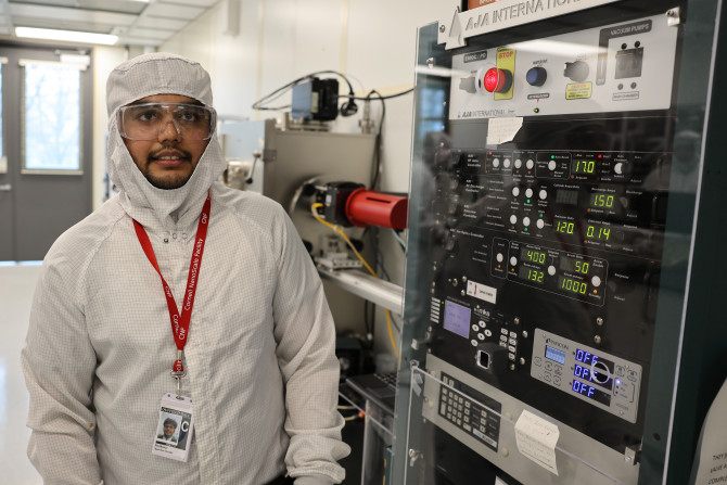 student in a clean room stands next to equipment