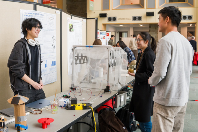 three students stand at a table with devices