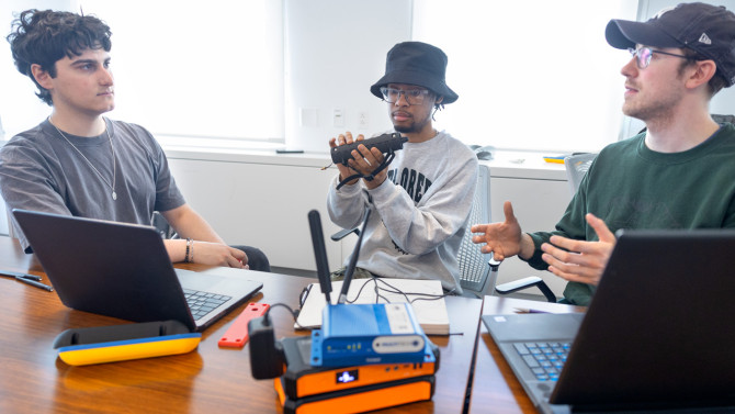 Duffield Engineering students Andrew D’Onofrio ’26 (left) and Jamison Taylor Jr. ’26 (center, holding the baton) discuss their tracking baton project with teammate and master’s student Kobe Phillips.
