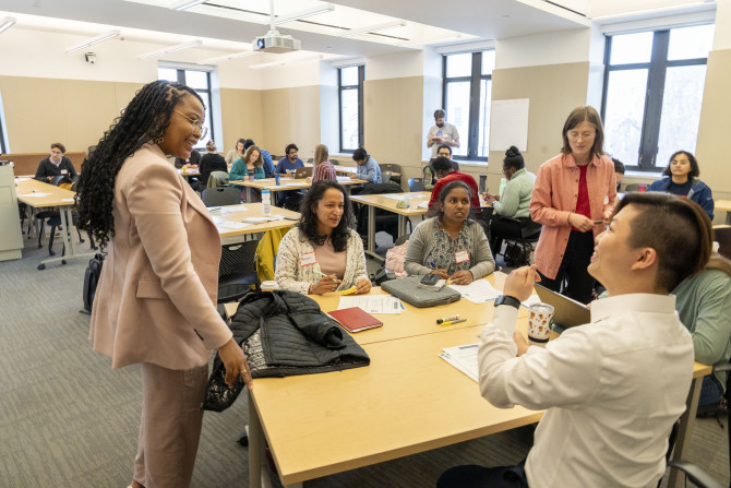Two graduate teaching fellows converse with a table of four graduate students at a conference