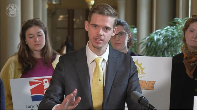 Cole Laudenslager speaking at a press conference podium alongside lawmakers and the New York Coalition for Open Government