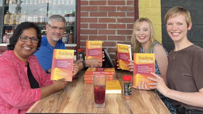 The four editiors of Teaching Graduate pose for a photo around an outdoor table. 