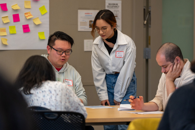 A graduate teaching fellow, checks in  on a breakout session of three graduate students at a table.