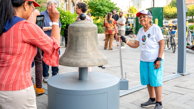 A visitor tolls the 600-pound bronze bell at the base of “Let Freedom Ring”