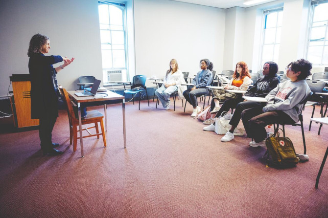 Person stands in front of a small class, gesturing