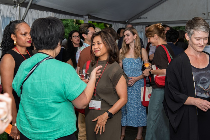 Several people stand together chatting during a reception event under a tent
